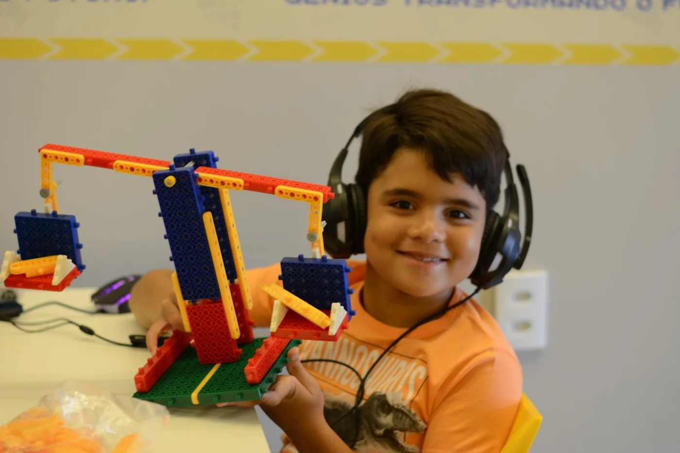 Aluno da Microbot sorrindo ao lado de uma montagem que construiu na aula de robótica